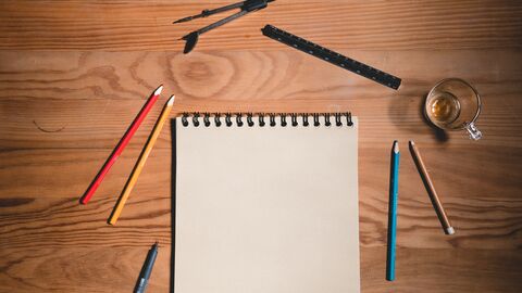 Holztisch mit Papierbogen und Zeichenwerkzeugen