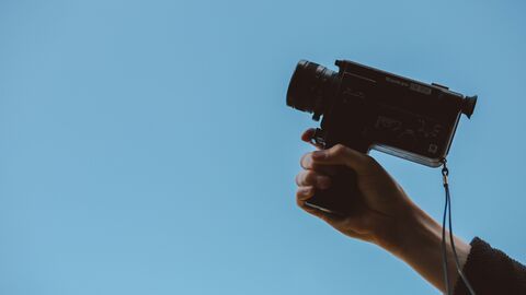 Kamera Person hält Videokamera vor einen blauen Hintergrund